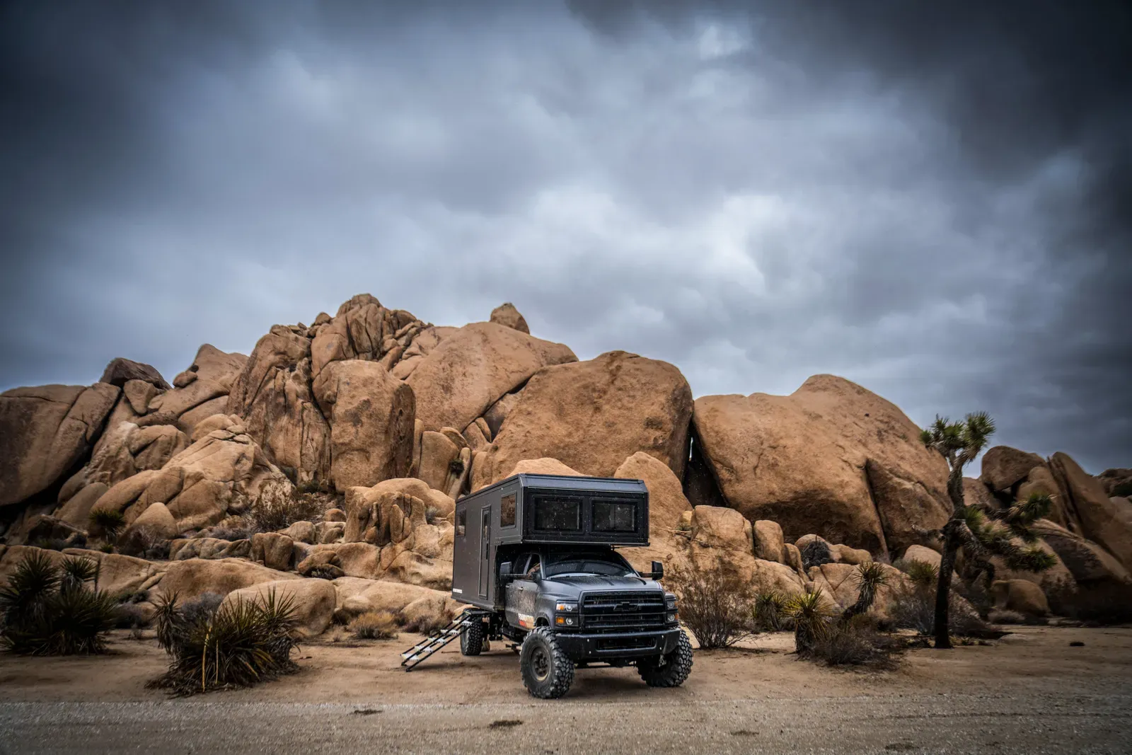 Blacked-out Chevrolet 6500 4x4 expedition camper on a desert road at golden hour near Joshua Tree