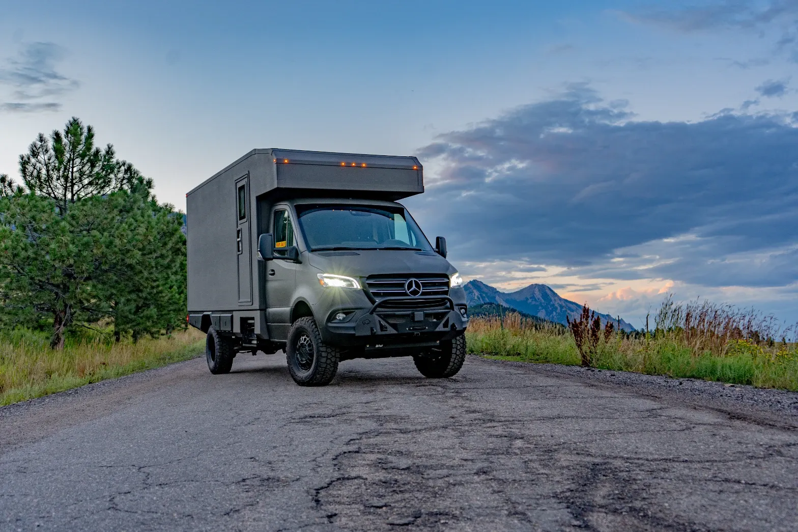 Matte-olive Mercedes-Benz Sprinter AWD composite camper at dusk with mountains behind