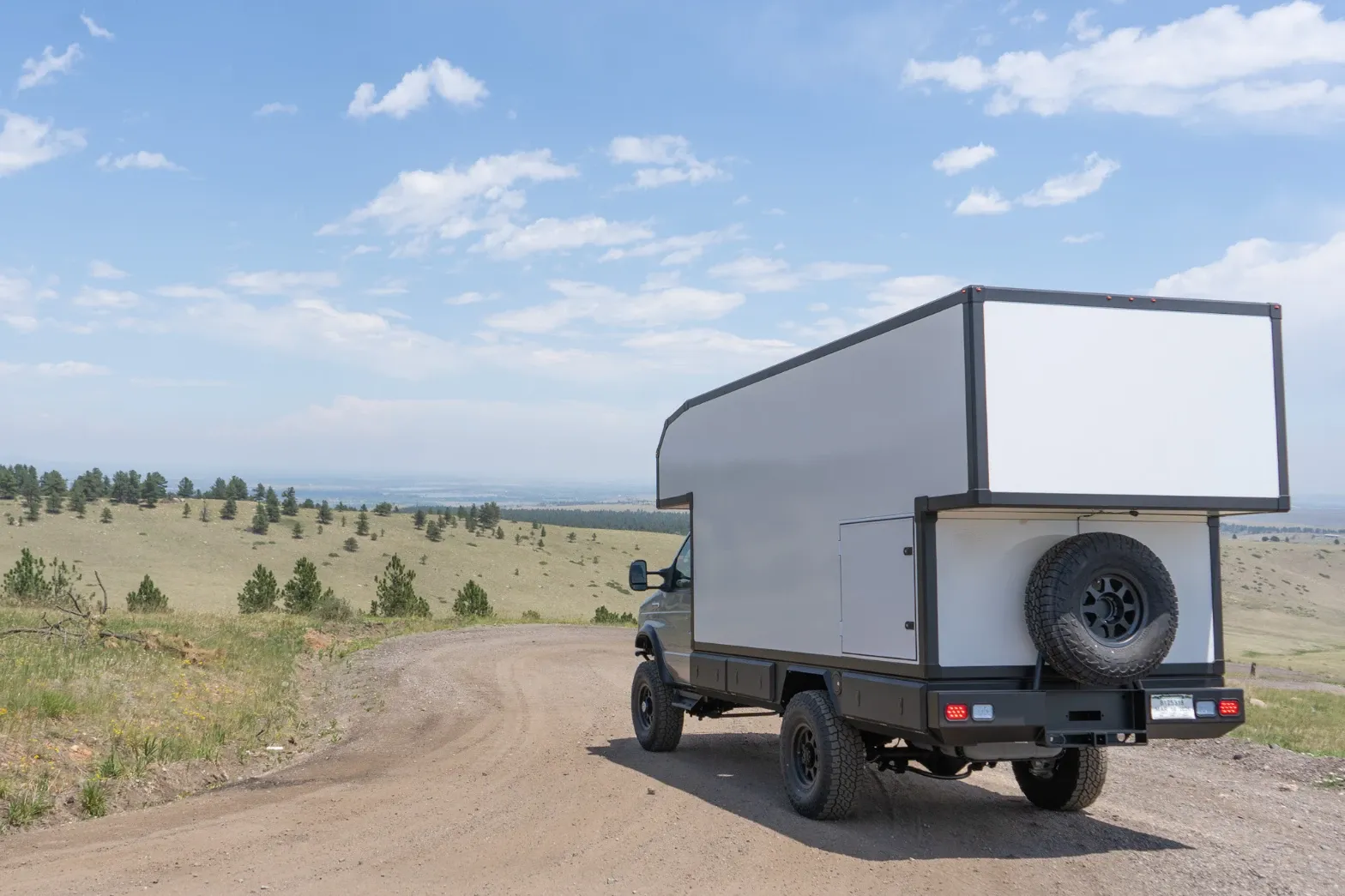 White Ford E-Series composite camper on a hilltop dirt road overlooking the plains