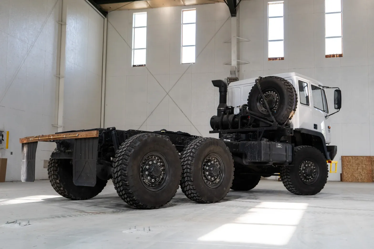 White 6x6 truck chassis, rear three-quarter view showing the bare frame ready for a body