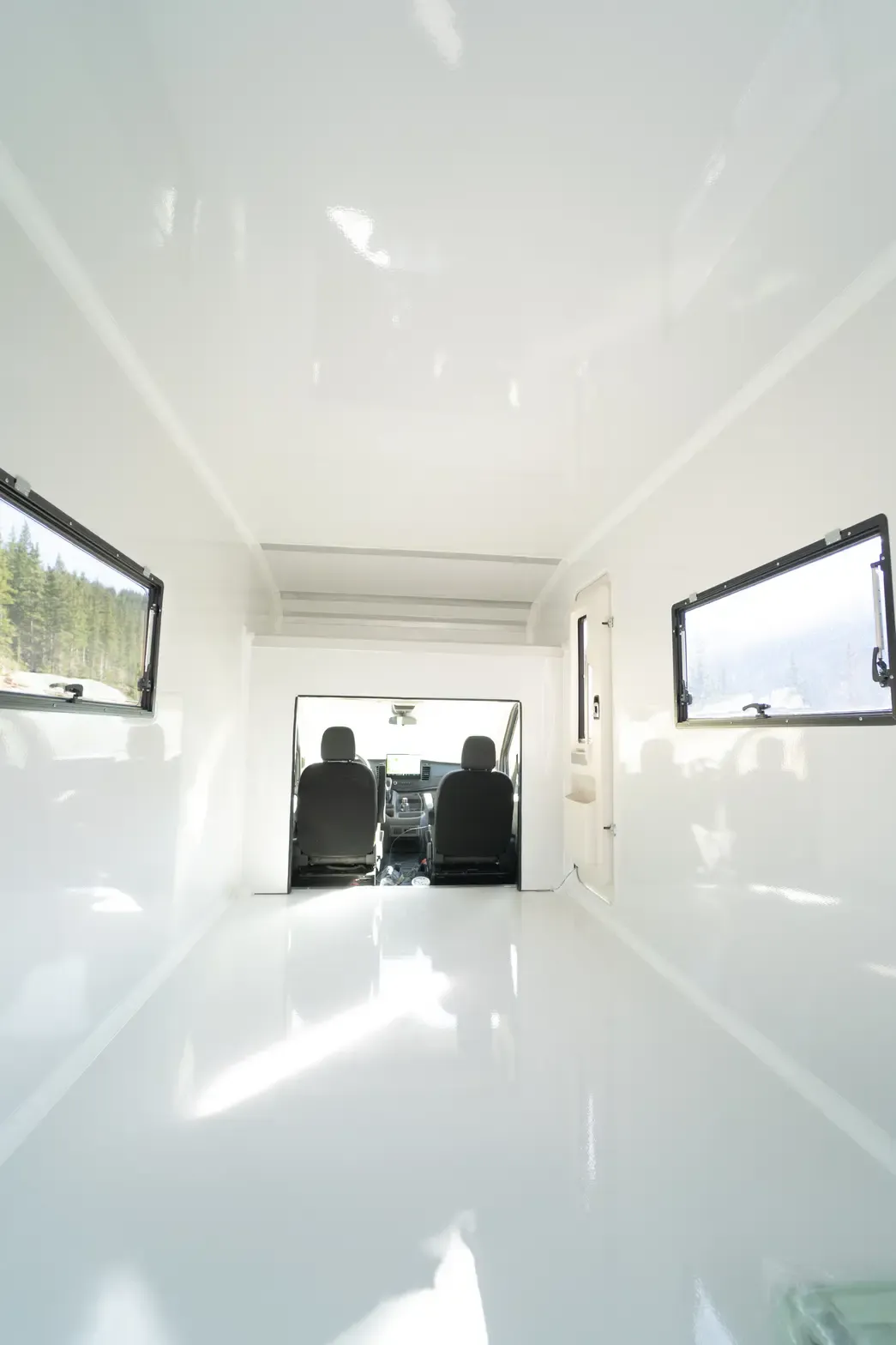 Interior of a bright white composite body looking toward the cab pass-through, with awning windows open on both walls