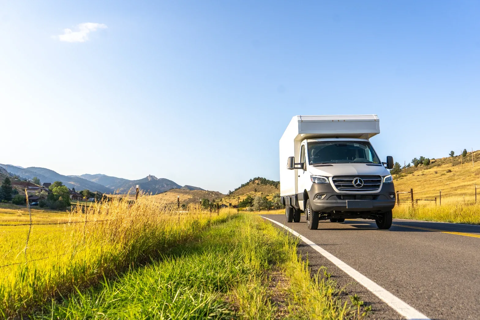 White Mercedes-Benz Sprinter composite camper on a rural highway toward the mountains