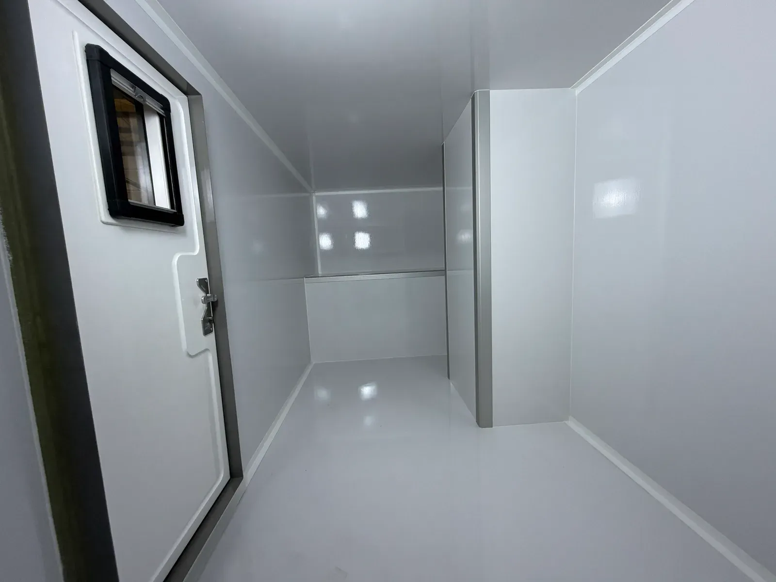 The full length of a finished white composite body — bright, seamless walls, a locking entry door with window, and a glossy wipe-clean floor