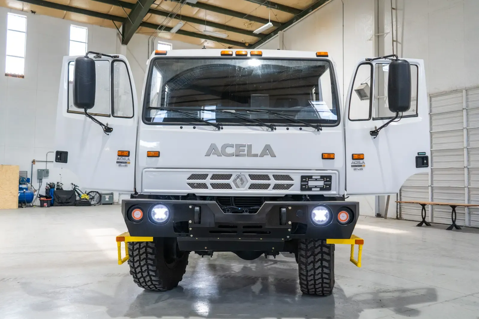 White Acela Monterra 6x6 cab-chassis, head-on view with the headlights on