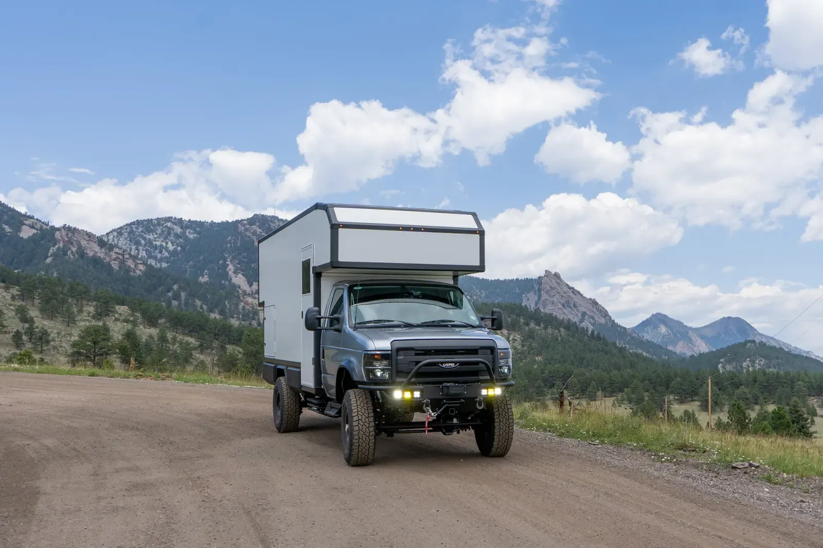 Silver-cab Ford E-450 expedition camper driving a dirt road with its headlights on