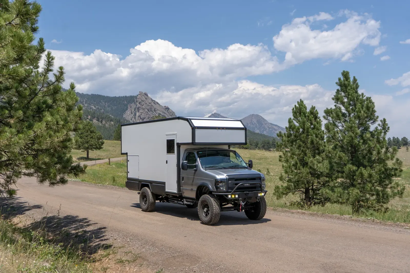 Silver-cab, white-cabover Ford E-450 expedition camper, side view parked in a mountain meadow