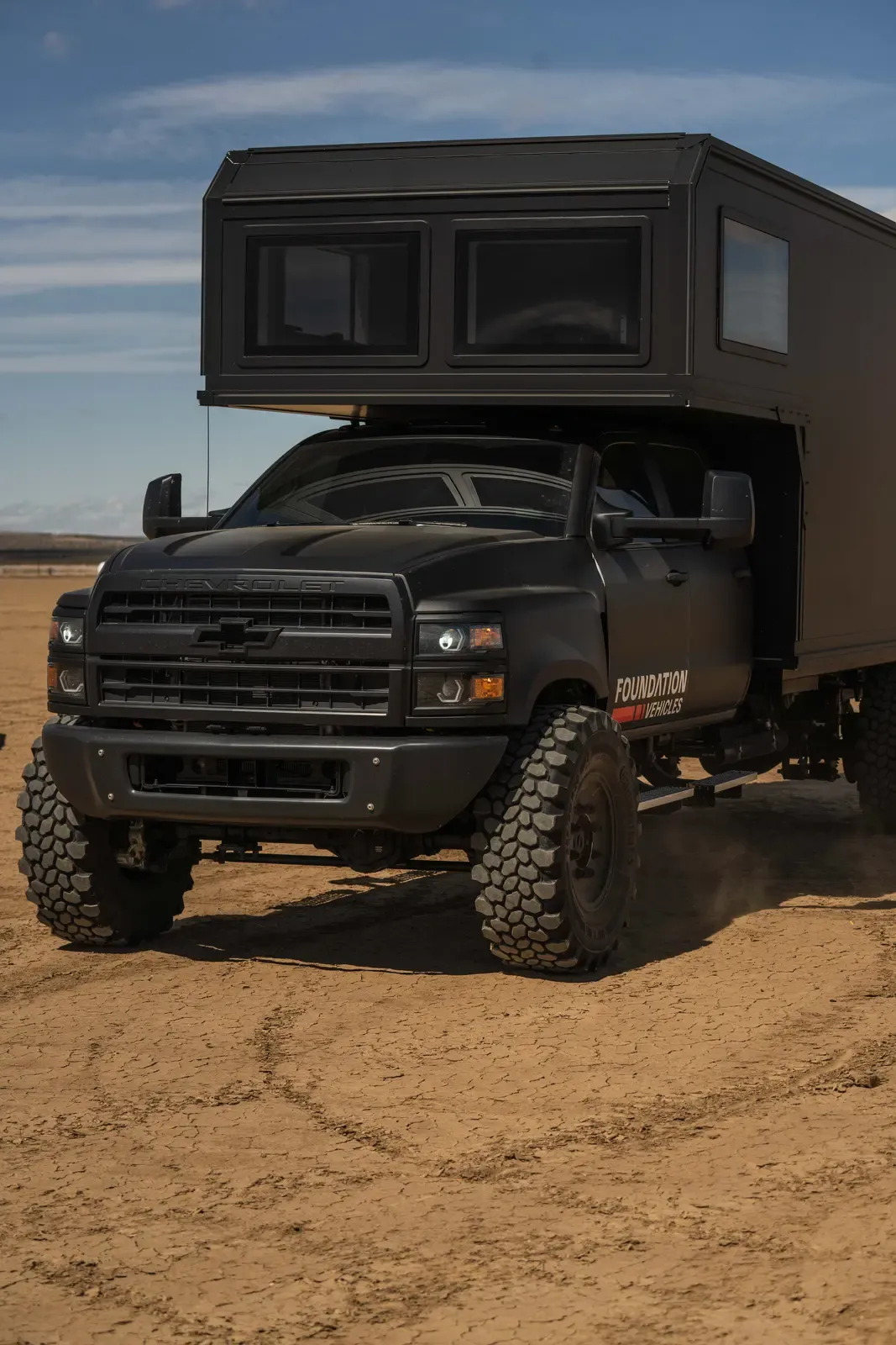 Blacked-out Chevrolet 6500 4x4 expedition camper, front three-quarter driver-side view in the desert