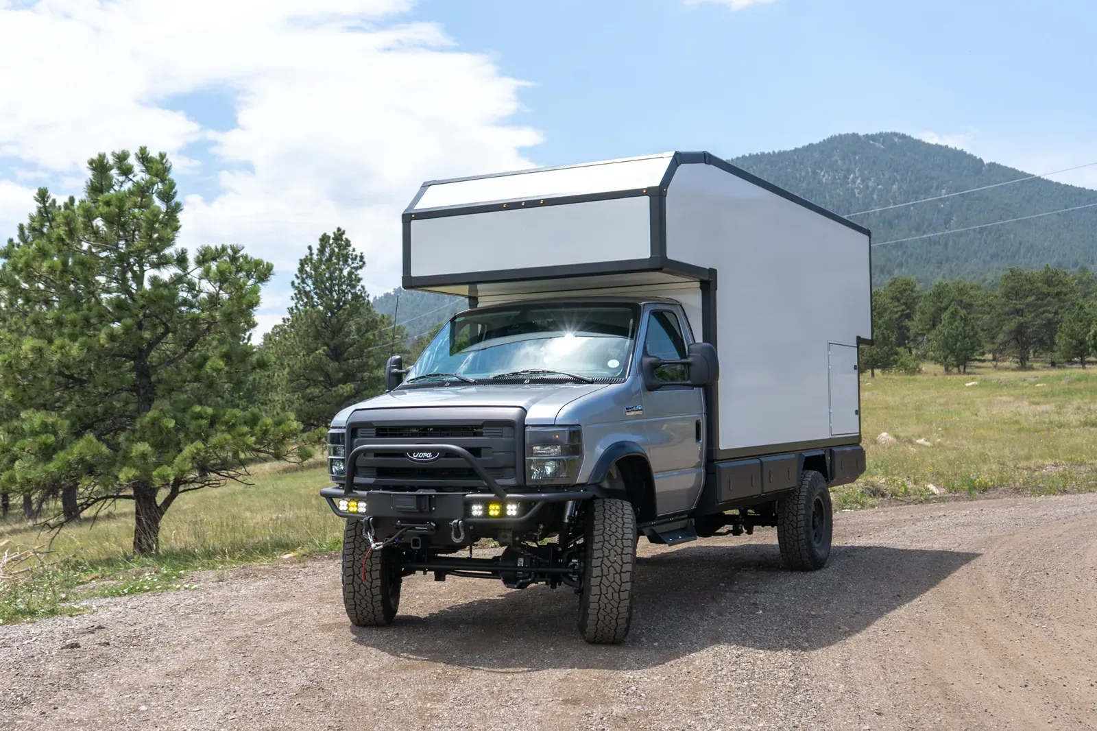 Ford E-450 4x4 composite box camper, front three-quarter on a mountain dirt road