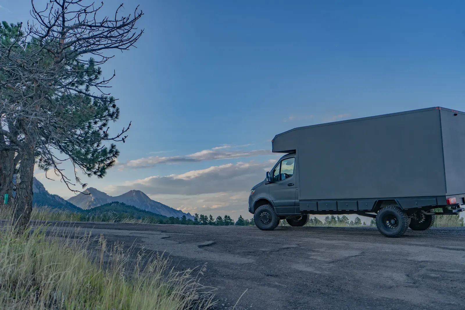Matte-olive FV-170 demo composite camper on a Mercedes-Benz Sprinter 170, side profile beside a pine at dusk