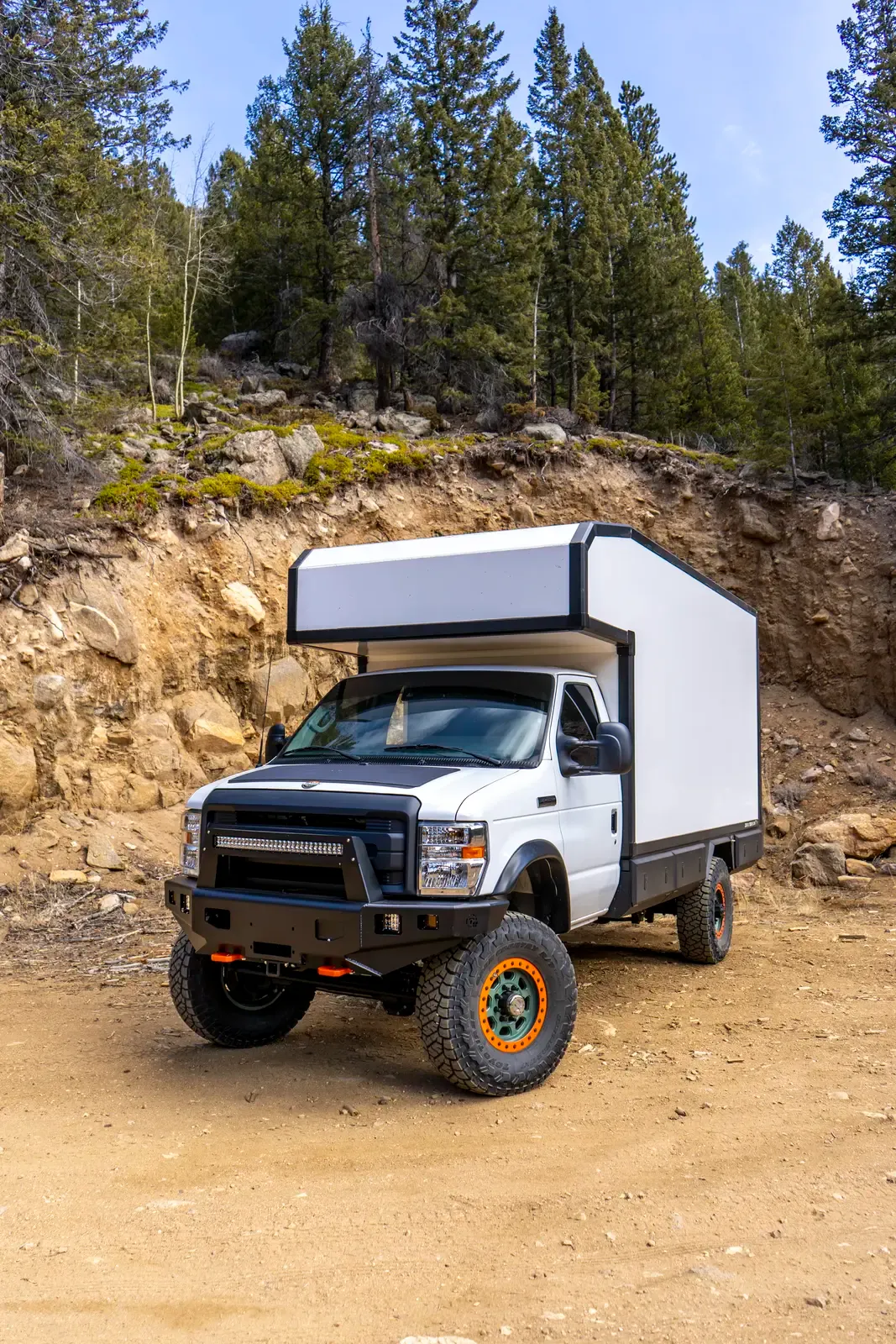 White E-158 composite box camper on a lifted Ford E-Series 4x4, front three-quarter view showing the off-road bumper and beadlock wheels