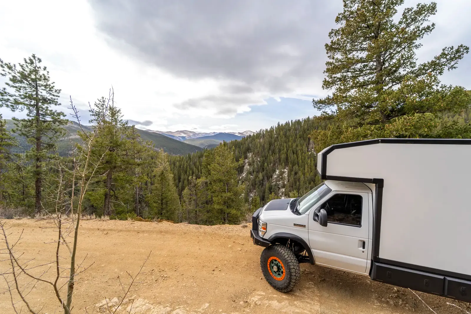 White E-158 composite box camper on a Ford E-Series 4x4, front three-quarter view on an open gravel clearing