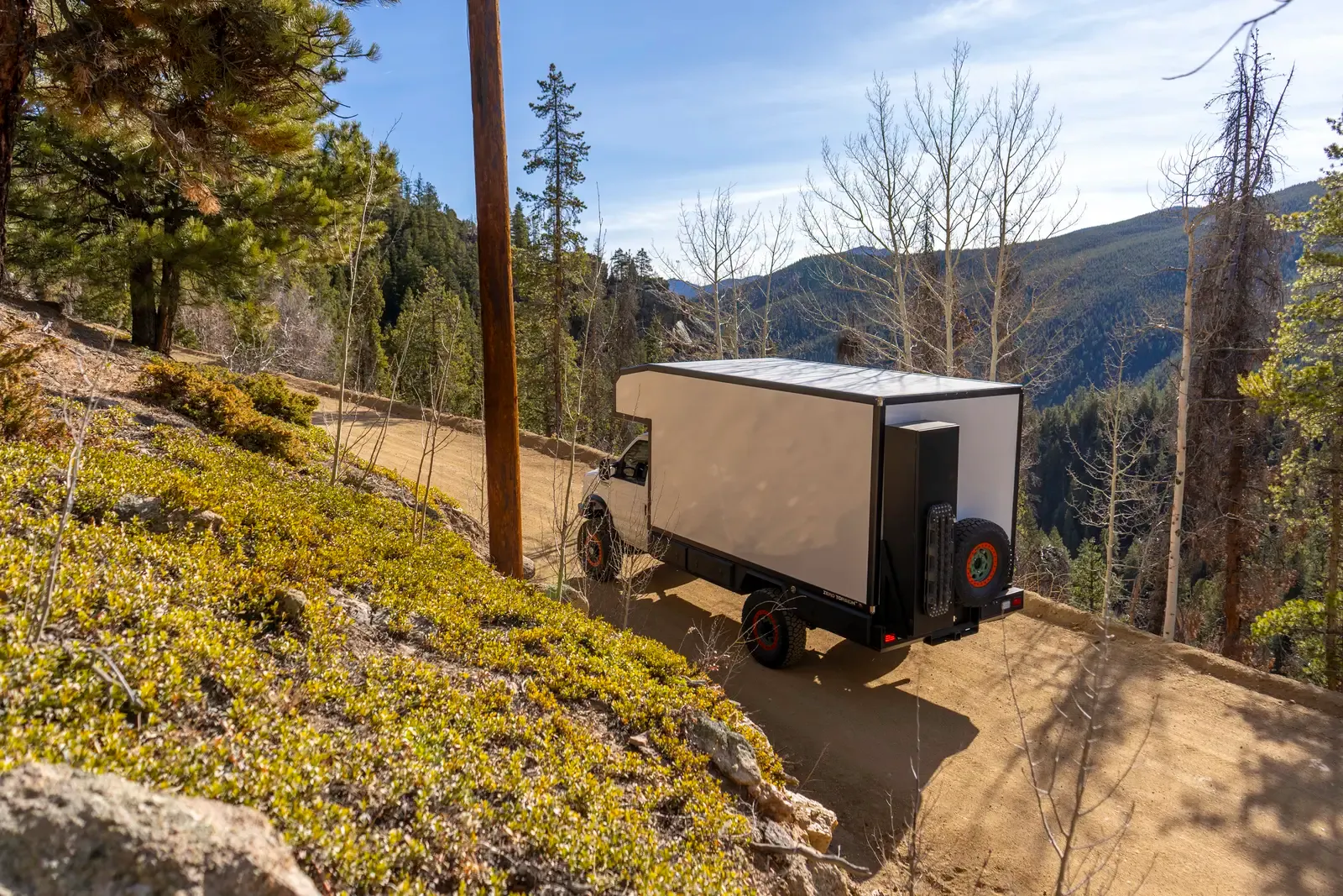 White E-158 composite box camper on a Ford E-Series 4x4, rear three-quarter view on a hillside ledge with mountains behind