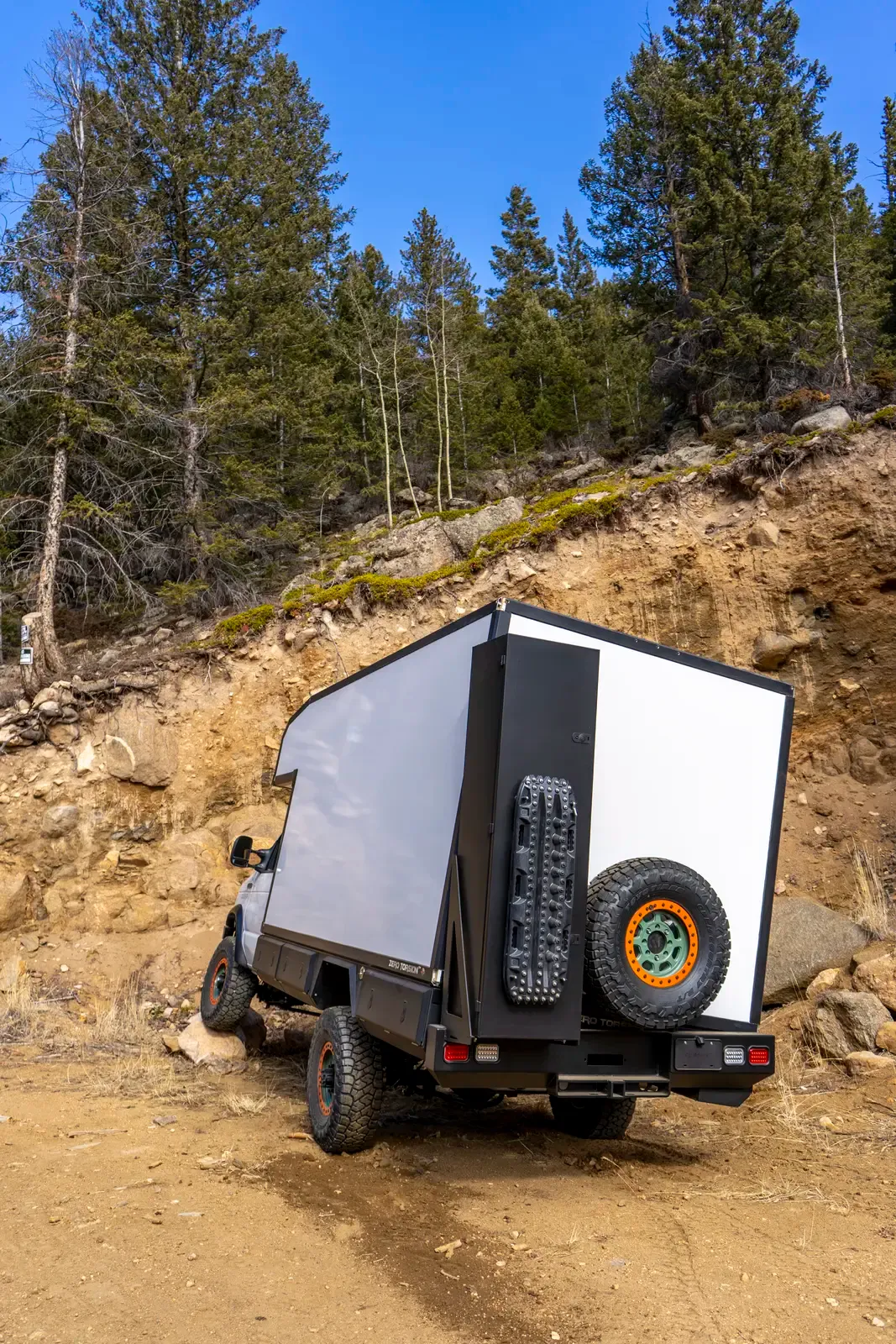 White E-158 composite box camper on a Ford E-Series 4x4 climbing a dusty off-road trail, rear three-quarter view