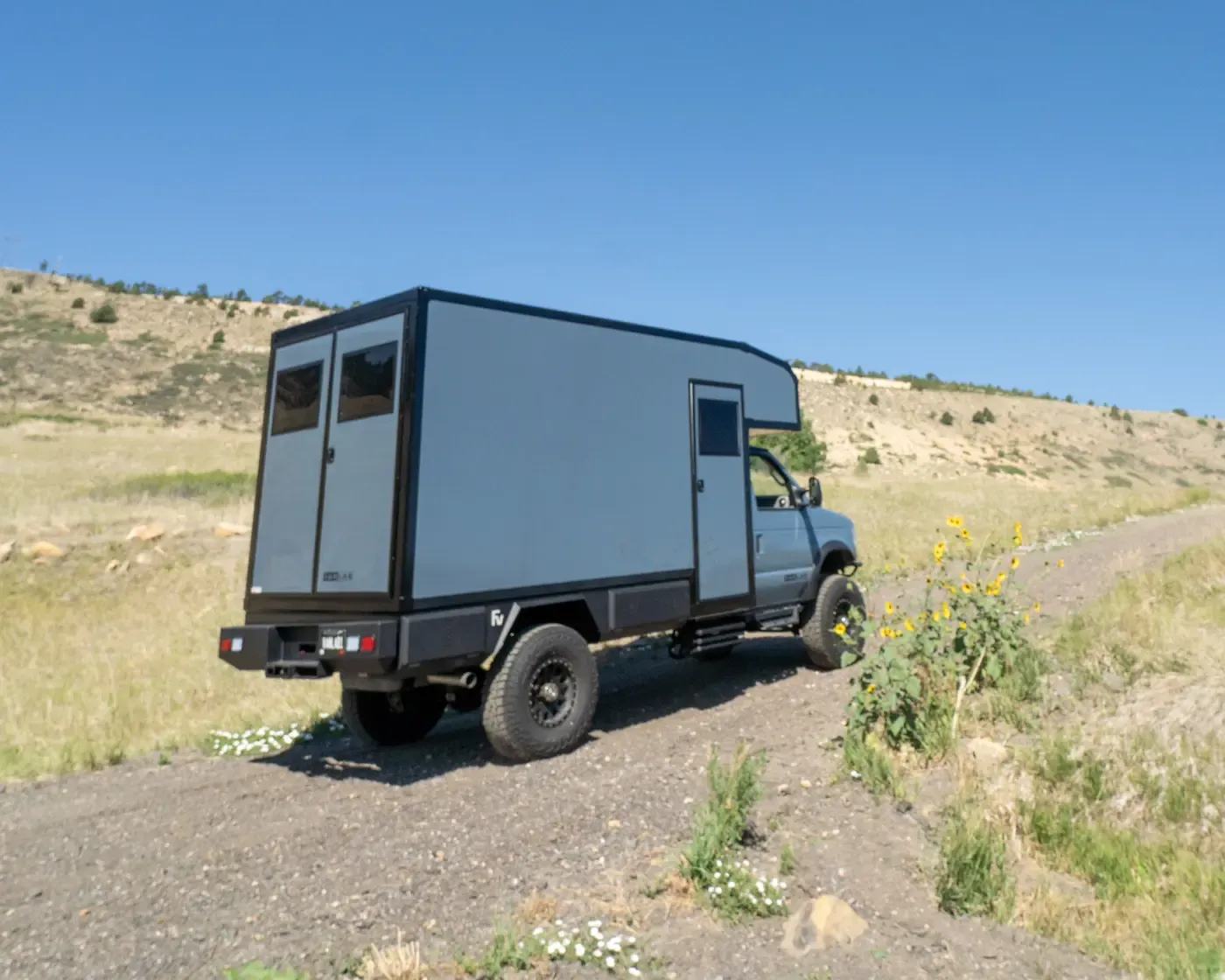 Foundation Vehicles E-158 composite box camper on the Ford E-Series 4x4 chassis, parked on a gravel road in open high country