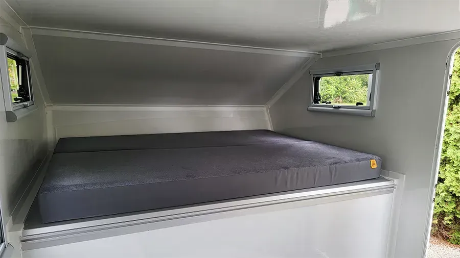 Inside a composite flatbed camper cabover — a queen mattress in the sleeping nook with an awning window