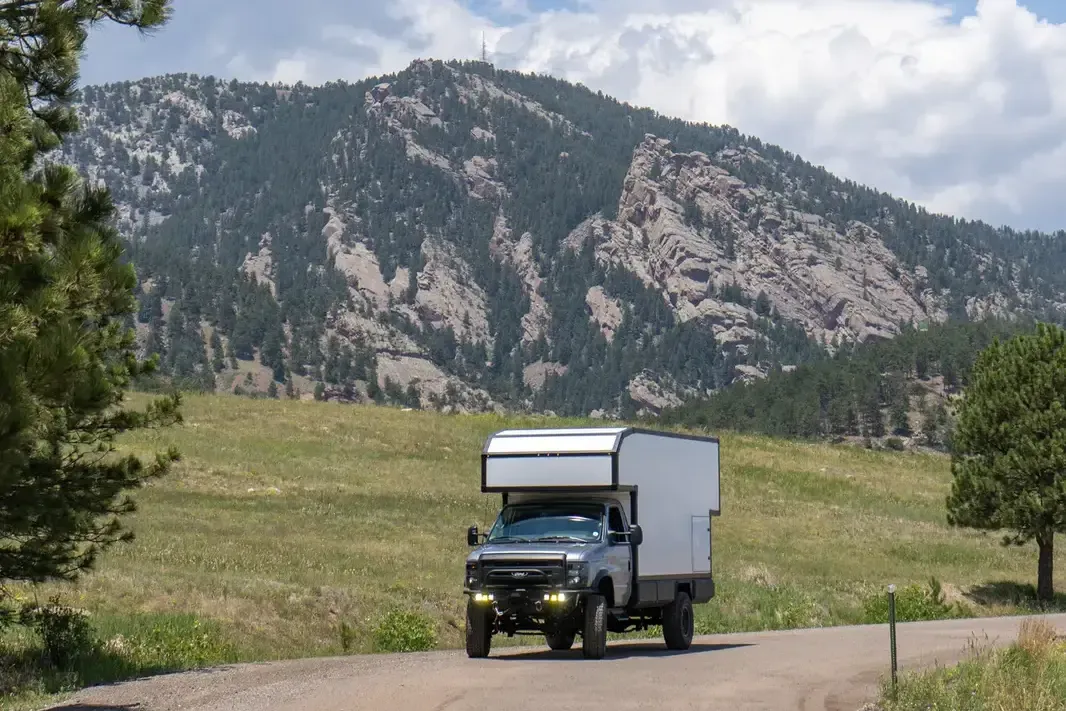 Ford E-450 4x4 custom expedition camper approaching on a dirt road with the foothills behind