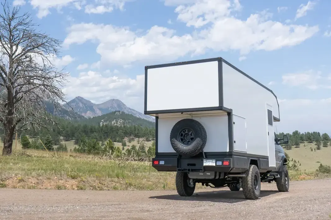 Ford E-450 4x4 custom expedition camper, rear three-quarter view showing the composite cabover body, rear alcove, and spare tire