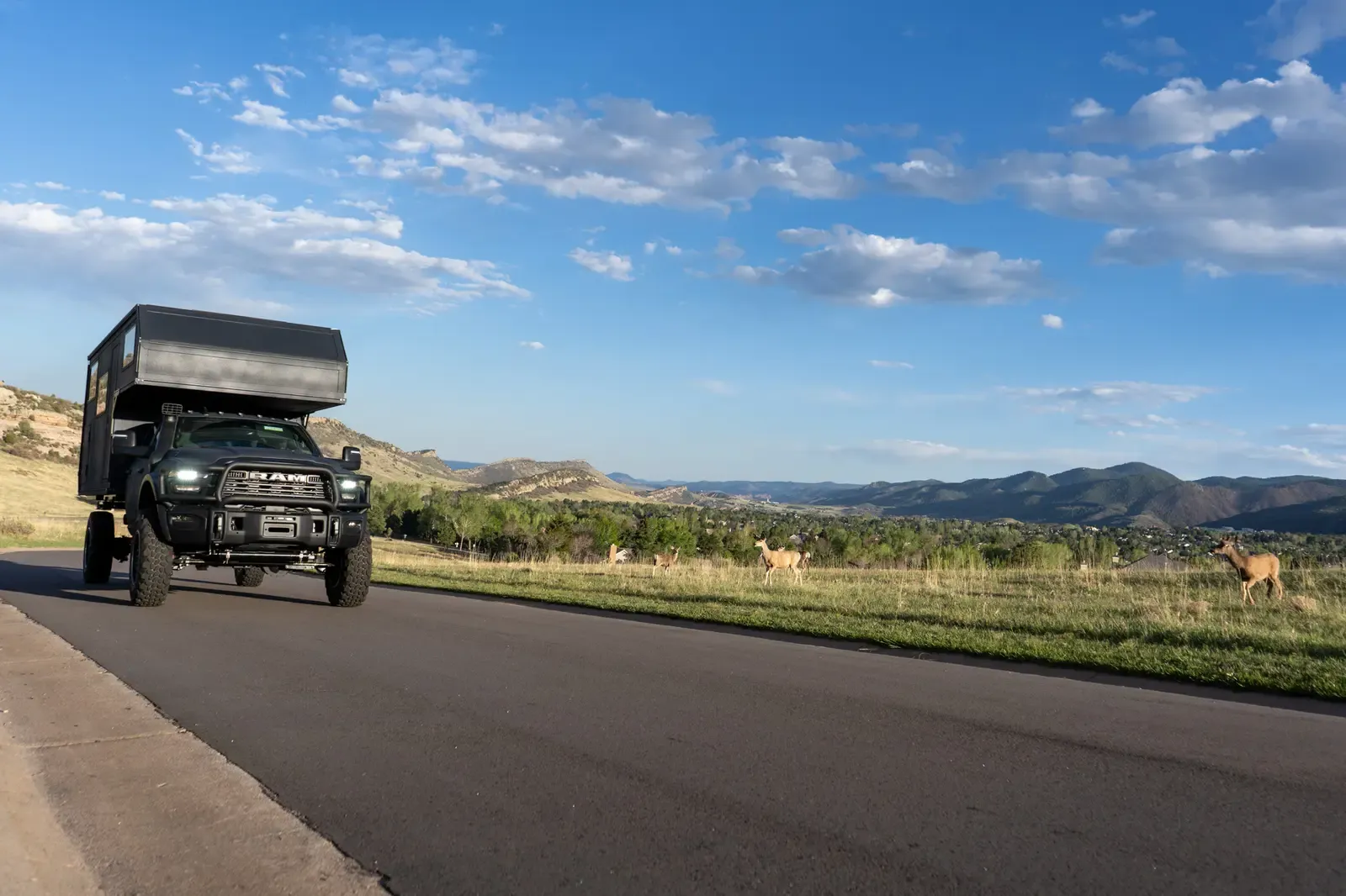 Black composite flatbed camper on a Ram 5500 cabover, front view on an open country road with mountains behind