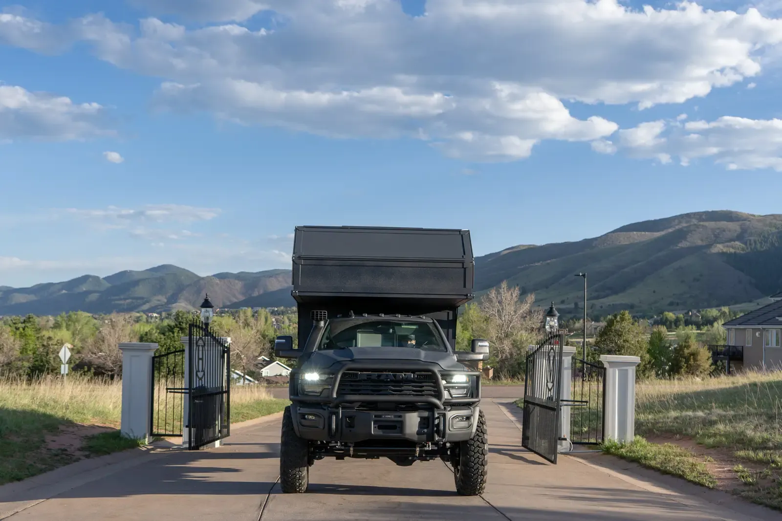 Black composite flatbed camper on a Ram 5500 cabover coming through an entrance gate with its headlights on