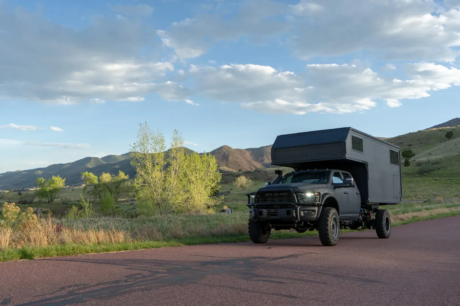 Black composite flatbed camper on a Ram 5500 cabover, three-quarter view with mountains behind