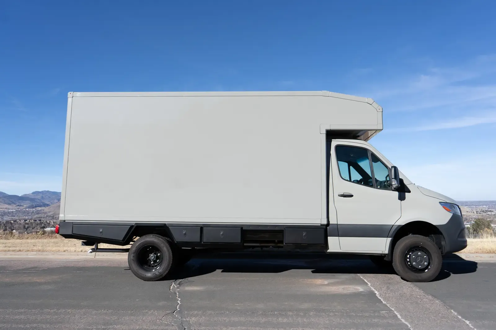 Stone grey commercial box body on a Mercedes-Benz Sprinter cab-chassis, side profile with the foothills behind