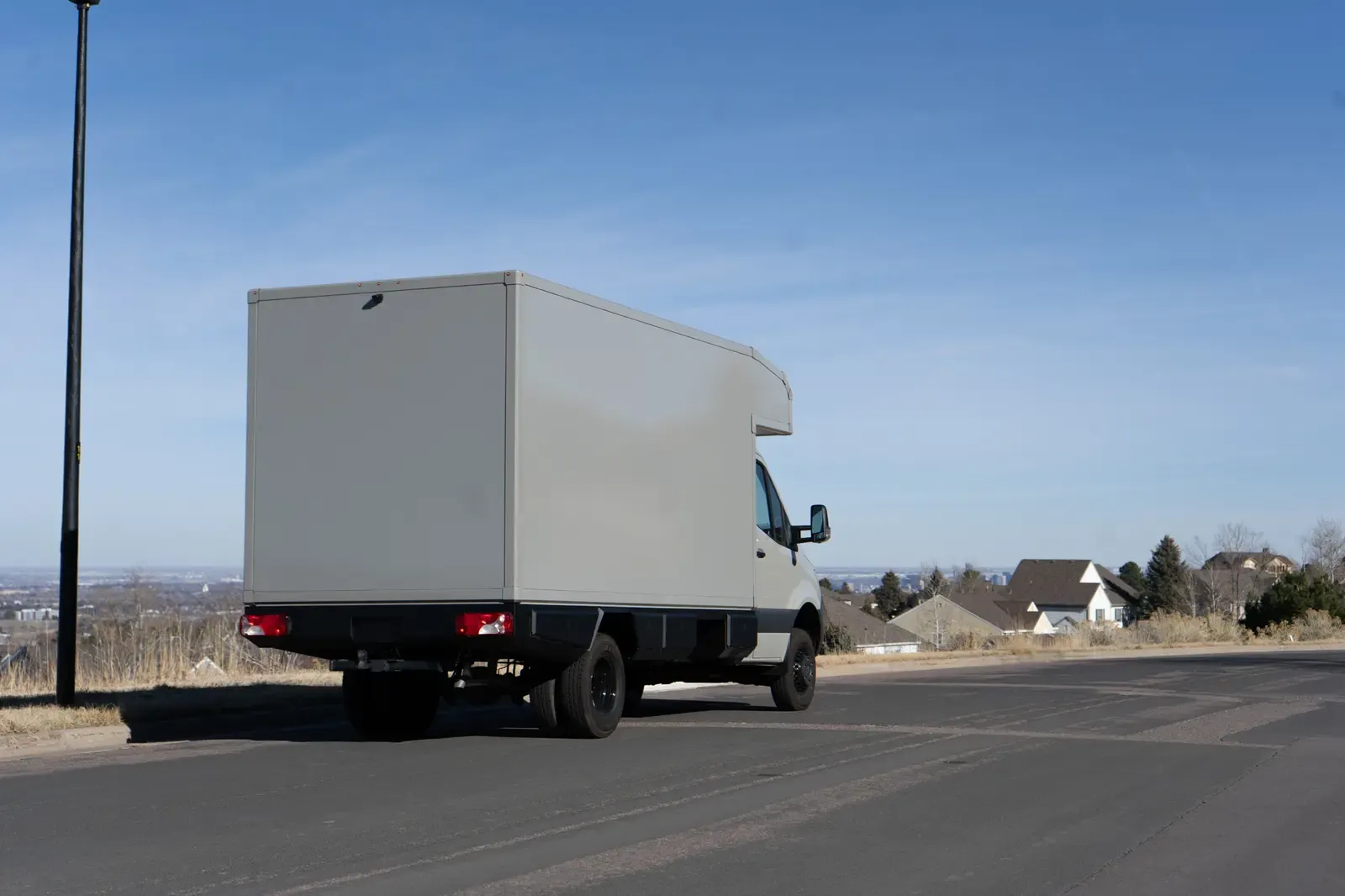 Stone grey commercial box body on a Mercedes-Benz Sprinter cab-chassis driving away on a country road