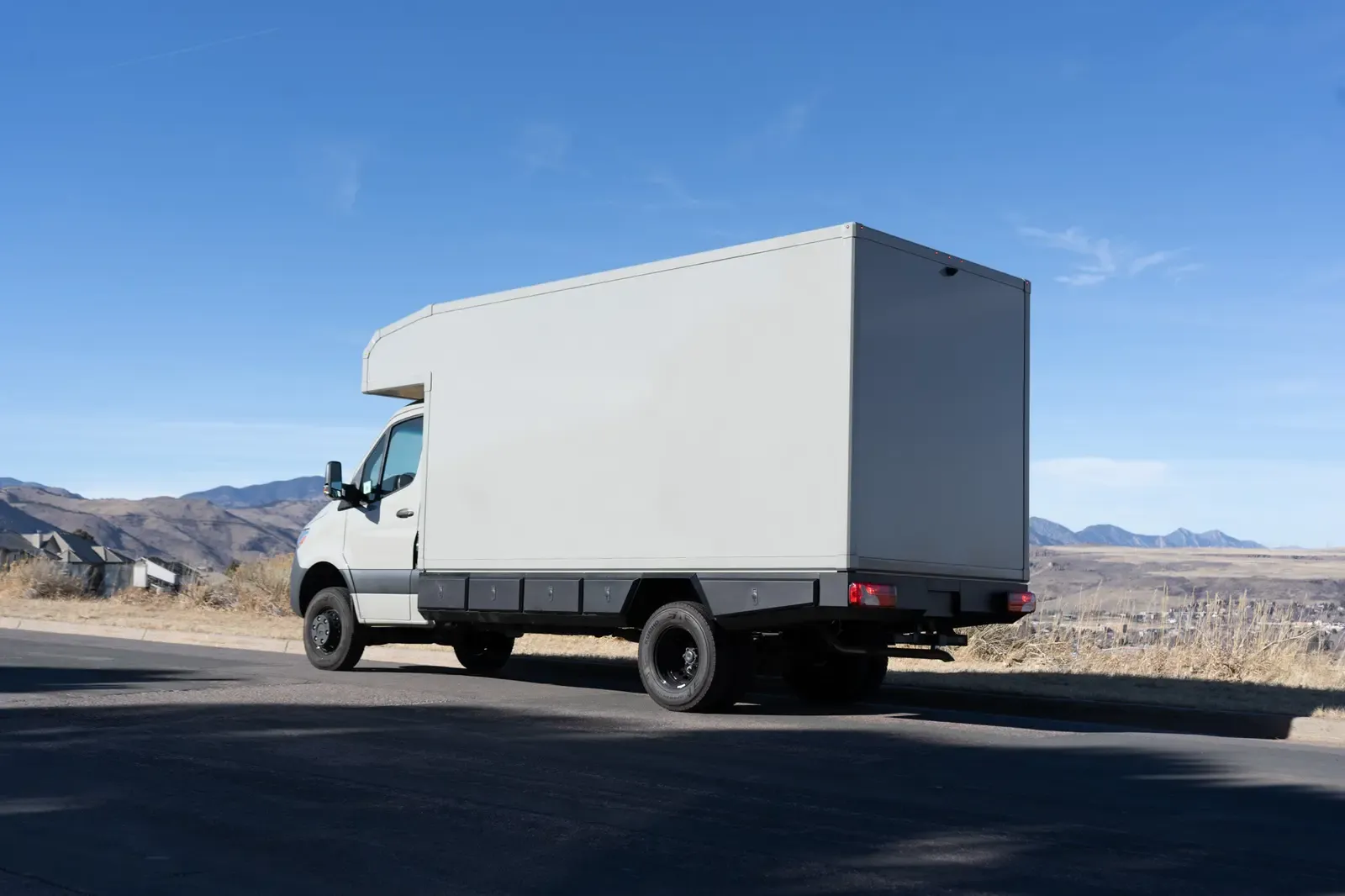 Stone grey commercial box body on a Mercedes-Benz Sprinter cab-chassis on a road with the foothills behind
