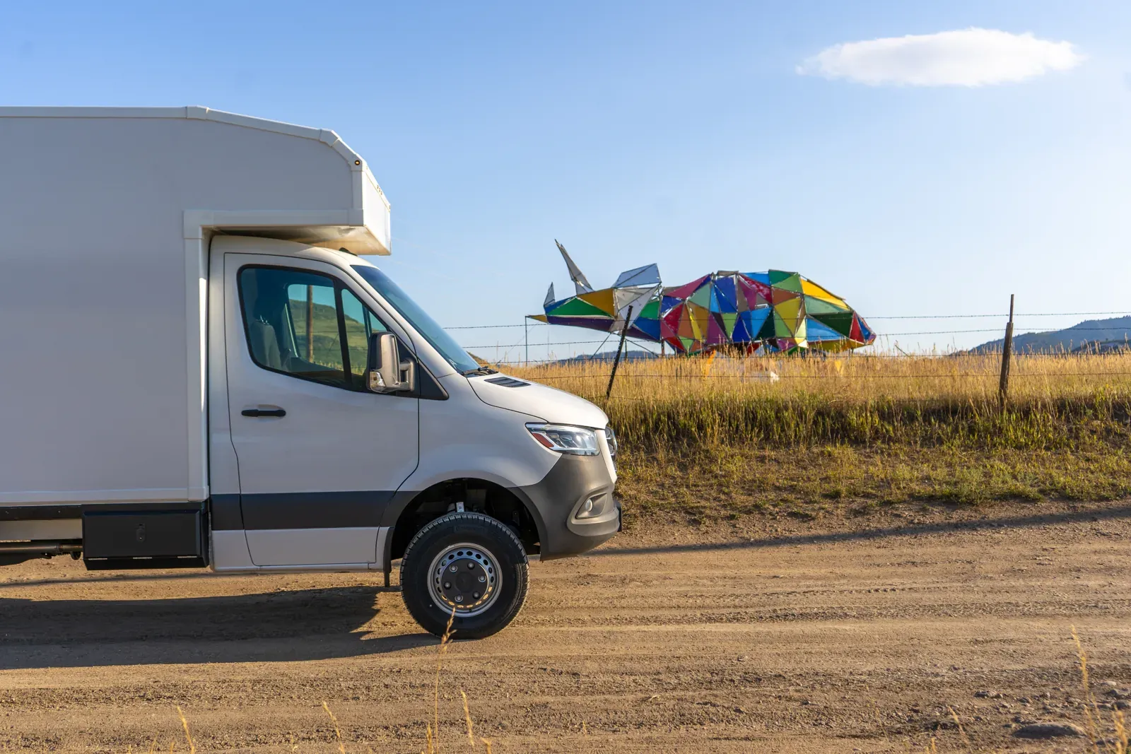 White Mercedes-Benz Sprinter 170 composite body with a roof rack, front three-quarter on a dirt road