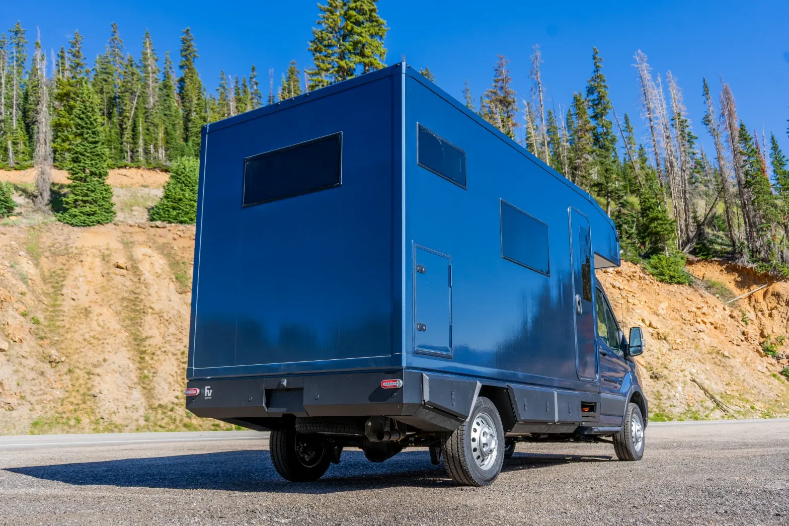 Blue composite box camper on a Ford Transit 156 AWD on a mountain pass, rear three-quarter view