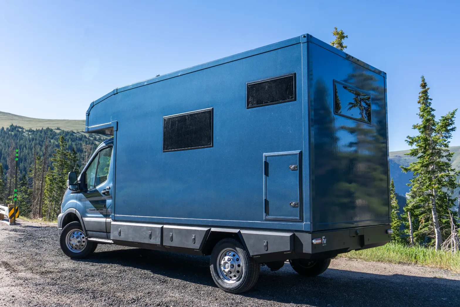 Blue composite box camper on a Ford Transit 156 AWD above an alpine valley, rear three-quarter view