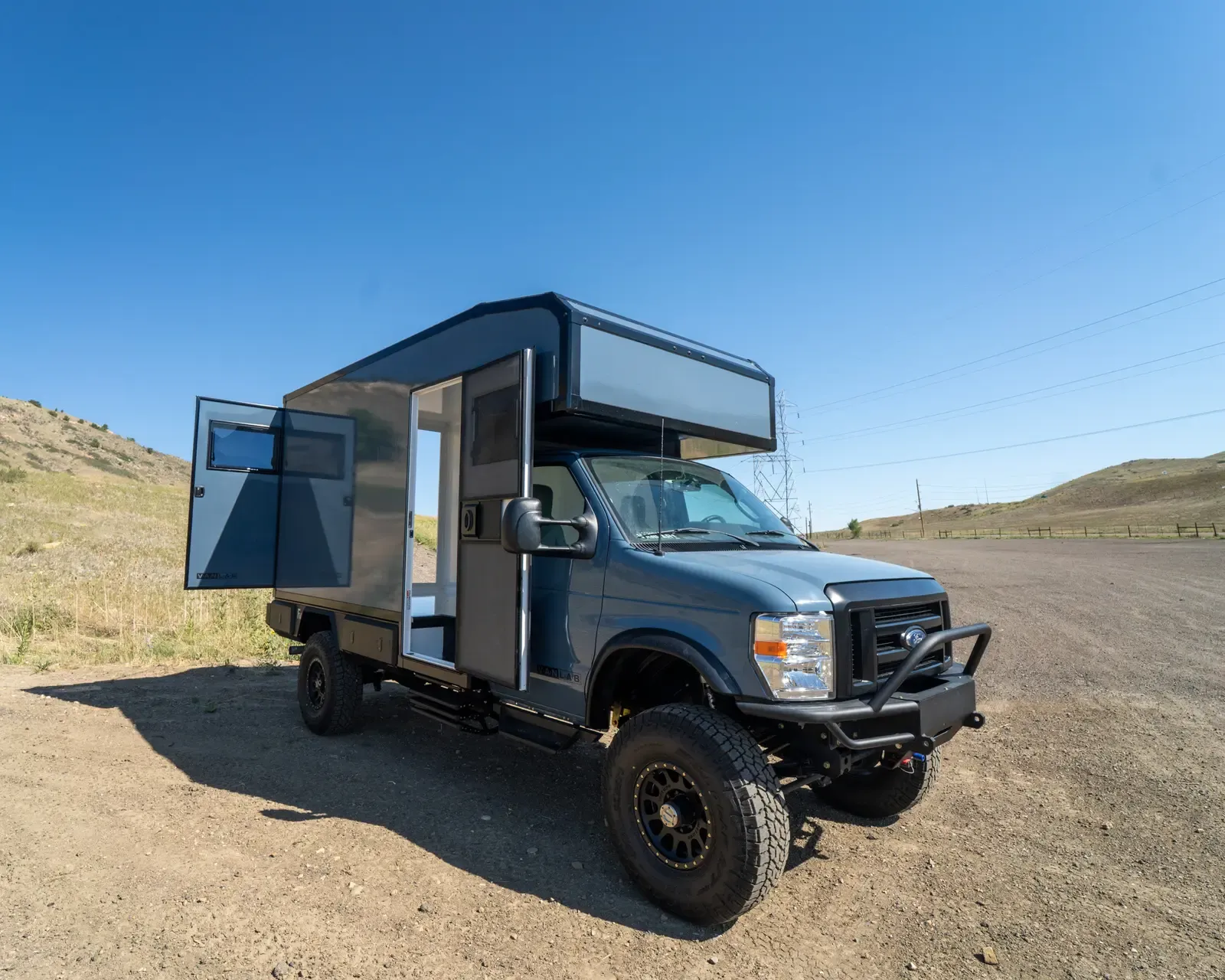 Two-tone composite camper on a Ford E-Series 4x4 with the entry door open, front three-quarter view