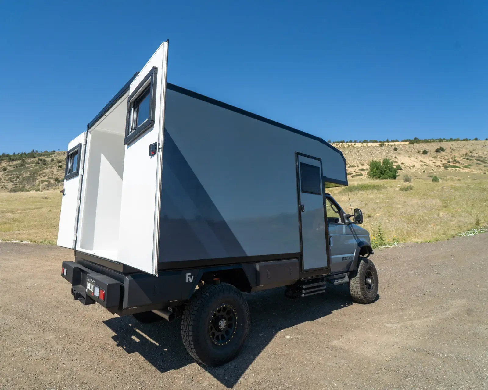 Grey-and-white composite box camper on a Ford E-Series 4x4, rear three-quarter view