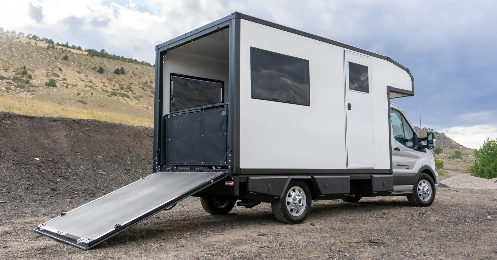 Foundation Vehicles RampDeck body on a Ford Transit 156 with the rear wall dropped into a flat deck and ramp to the ground and mesh side railings raised