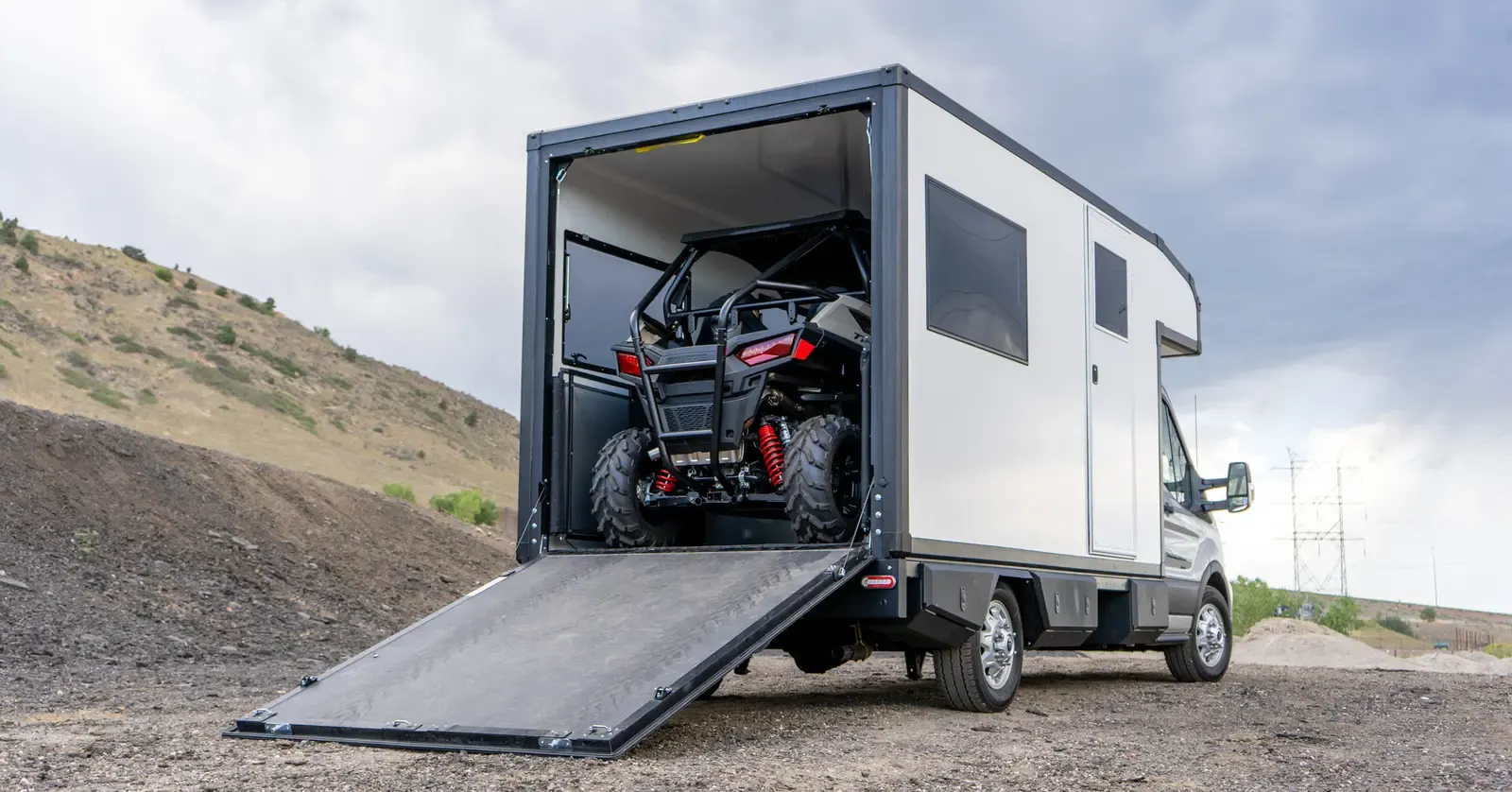 A side-by-side UTV loaded inside the garage of a Foundation Vehicles RampDeck body on a Ford Transit 156, rear ramp lowered to the ground