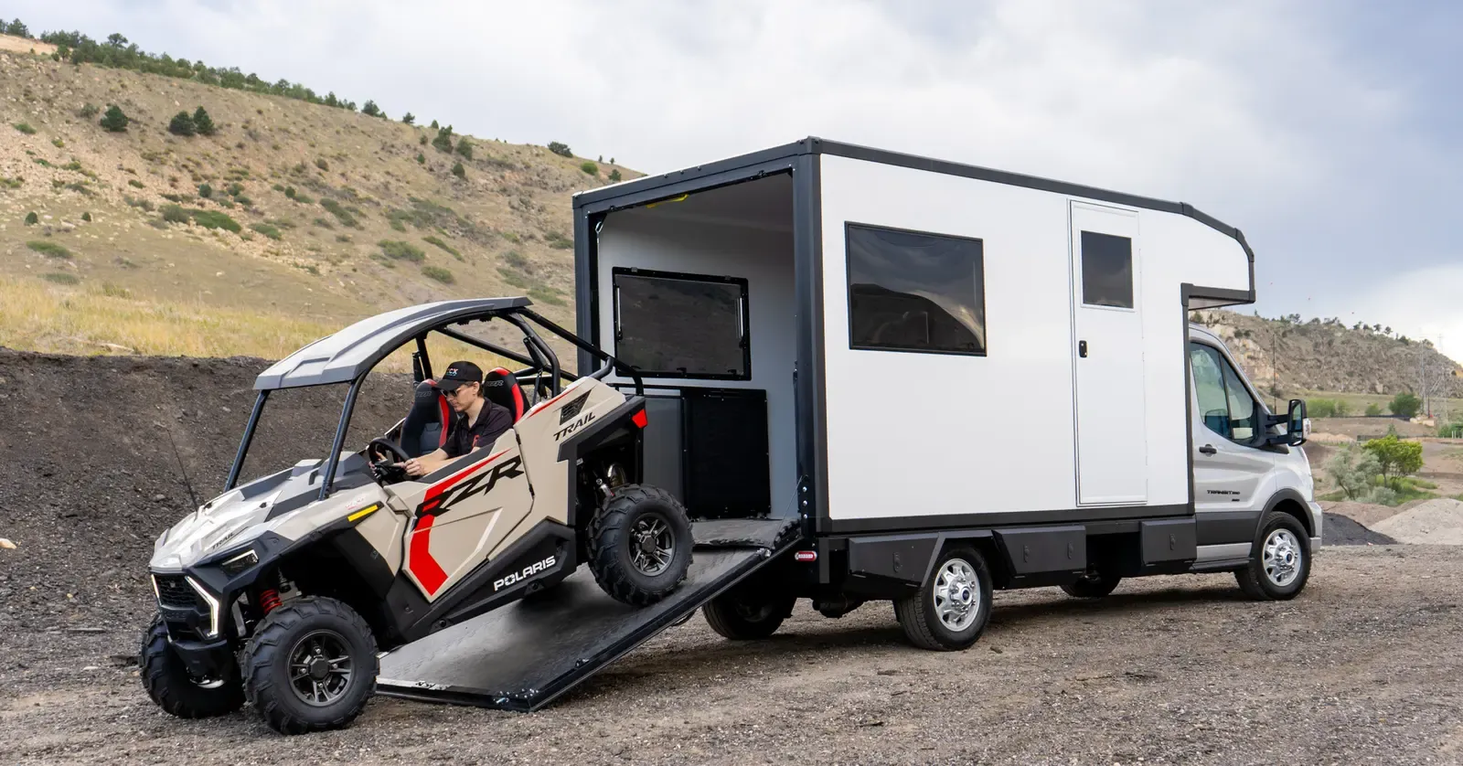 A Polaris side-by-side driving up to the lowered ramp of a Foundation Vehicles RampDeck body on a Ford Transit 156