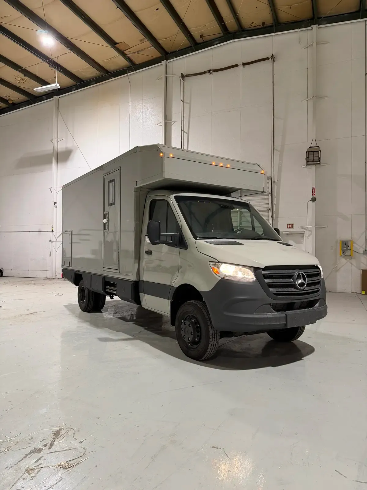 Grey commercial box body on a Mercedes-Benz Sprinter cab-chassis, front three-quarter view in the build shop