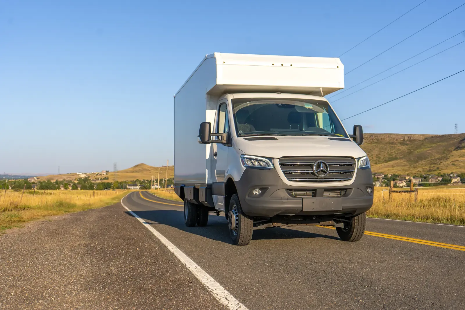 White composite box camper on an AWD Mercedes-Benz Sprinter 170, front three-quarter view on a sunlit country road