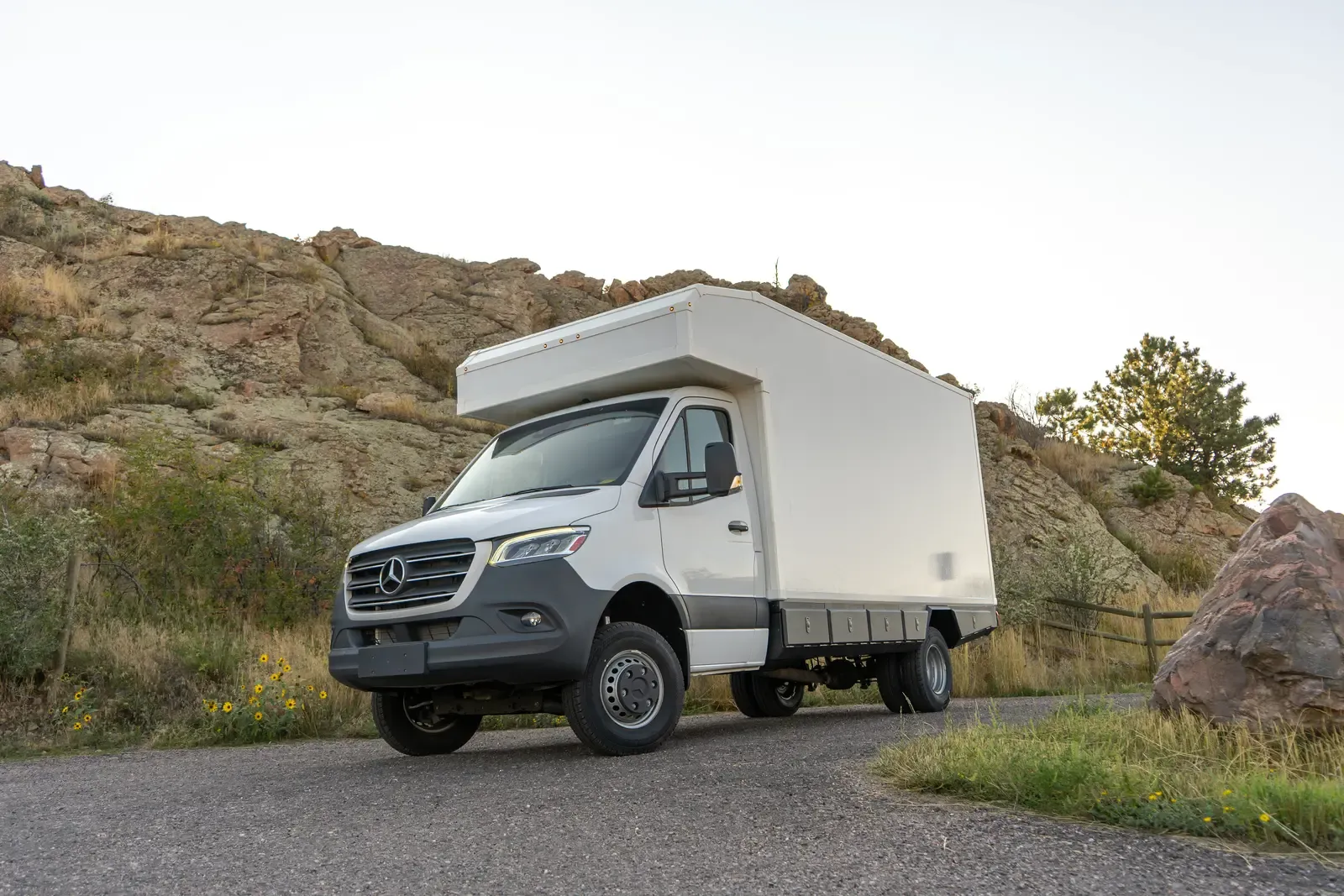 White composite box camper on a Mercedes-Benz Sprinter 170, front three-quarter view beside a red rock formation