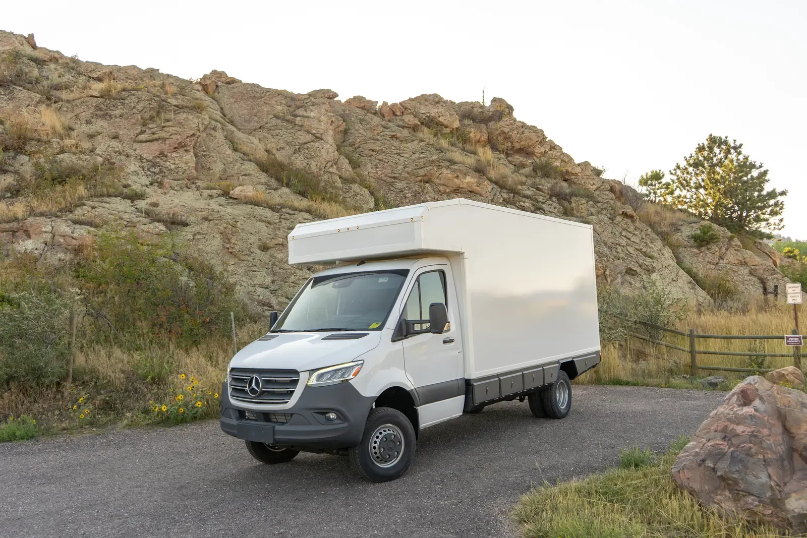White composite box camper on a Mercedes-Benz Sprinter 170, front three-quarter view below a rock outcrop