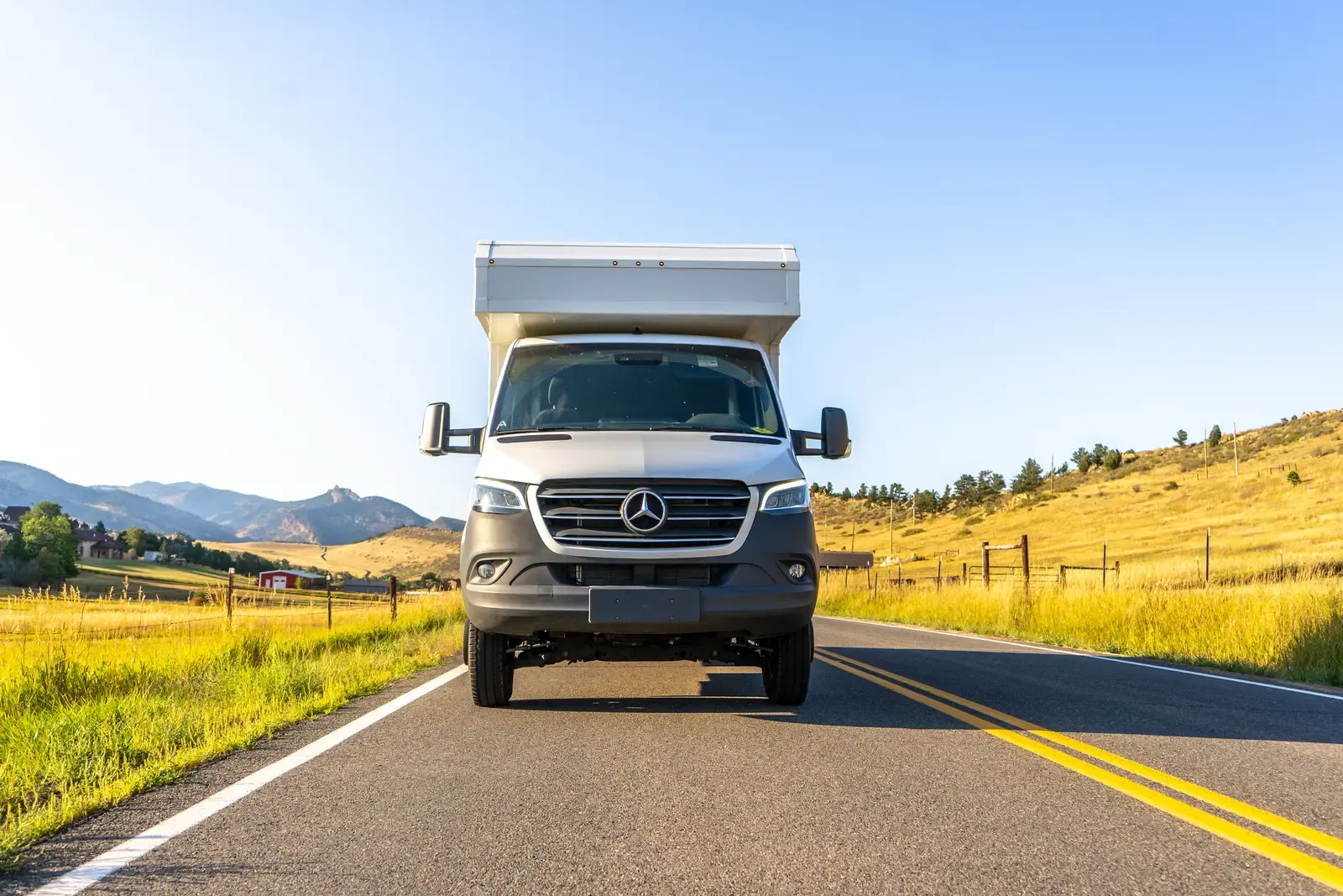 White composite box camper on a Mercedes-Benz Sprinter 170 on a mountain road, front three-quarter view