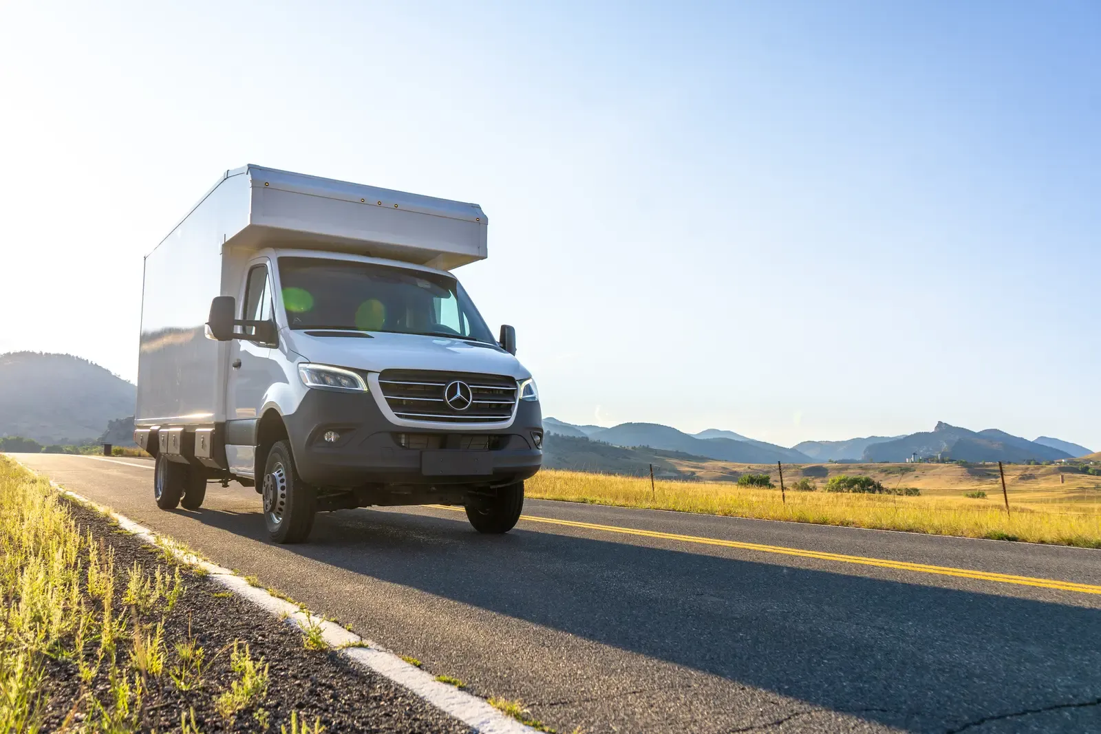 White composite box camper on a Mercedes-Benz Sprinter 170 on an open road with mountains behind