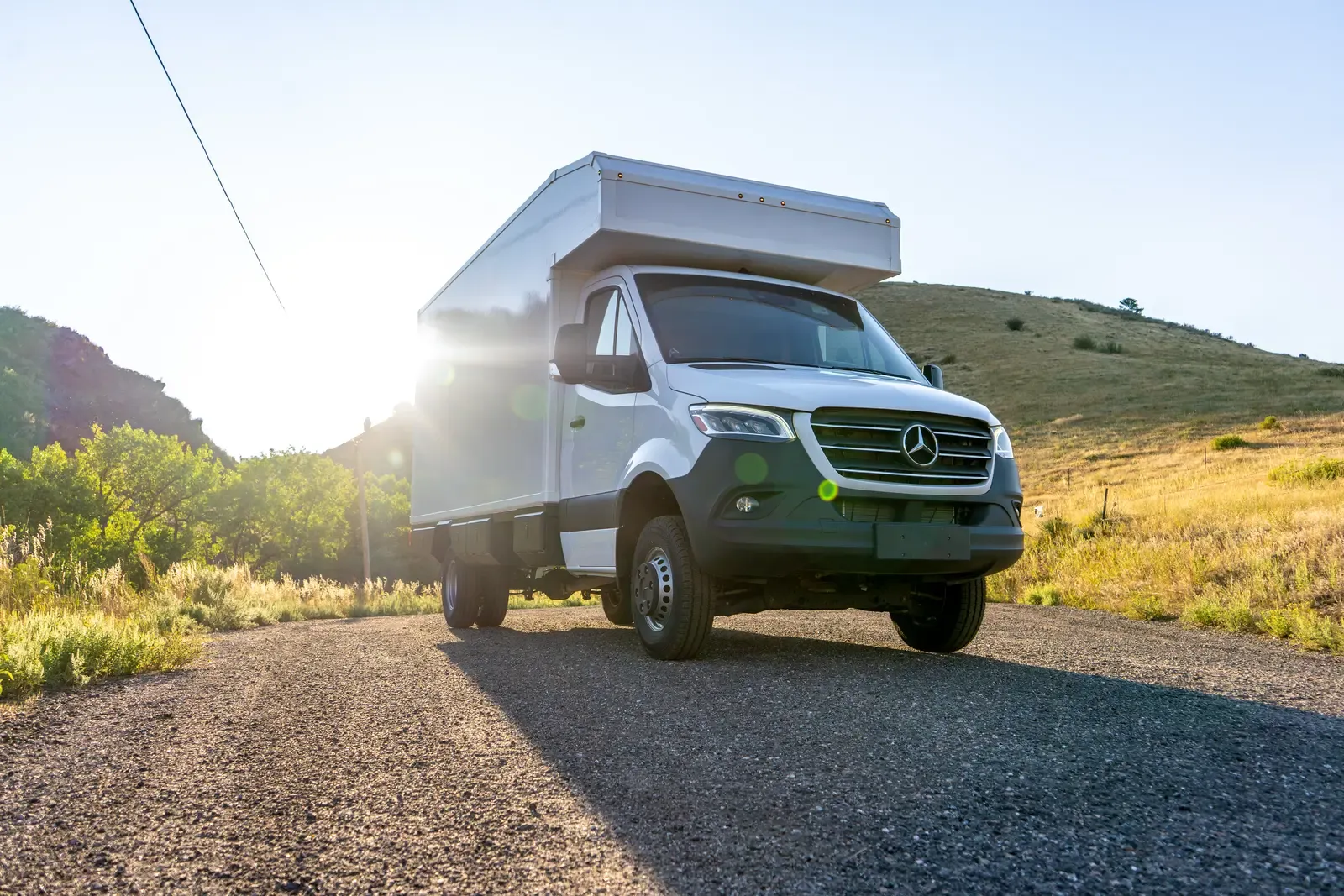White composite box camper on an AWD Mercedes-Benz Sprinter 170 on a road in golden backlight