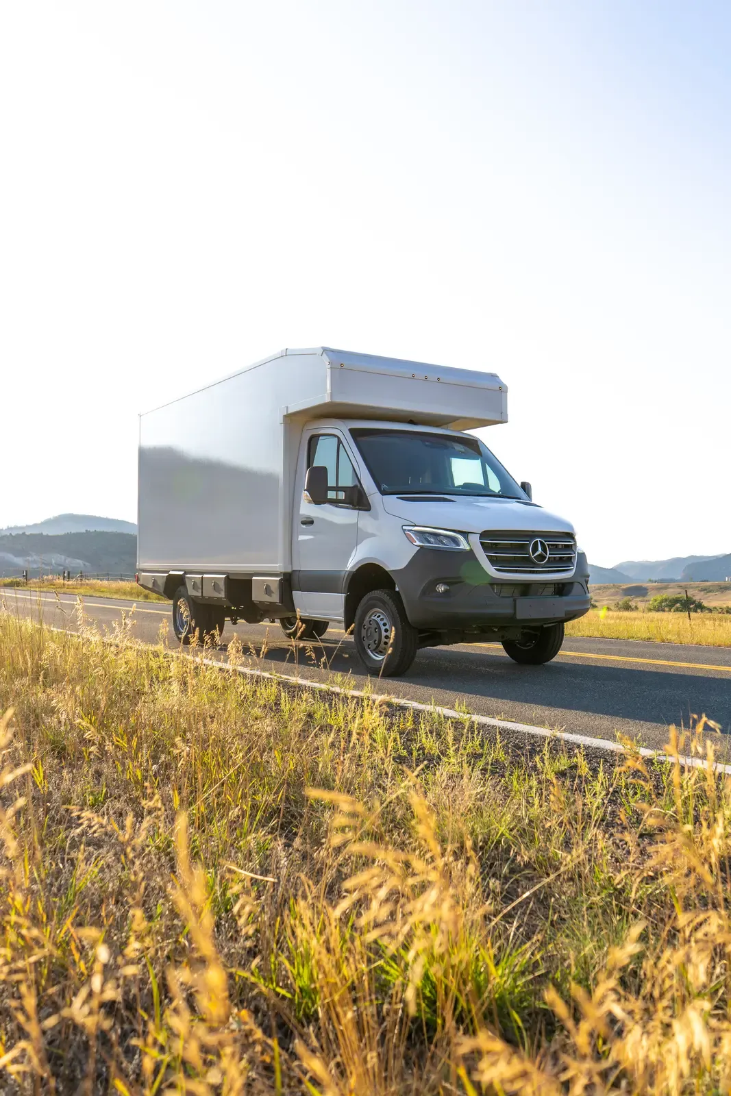 White composite box camper on a Mercedes-Benz Sprinter 170, front three-quarter view in golden evening light