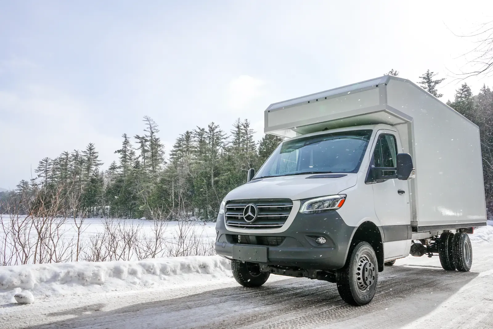 White composite box camper on a Mercedes-Benz Sprinter 170 by a frozen lake, front three-quarter view
