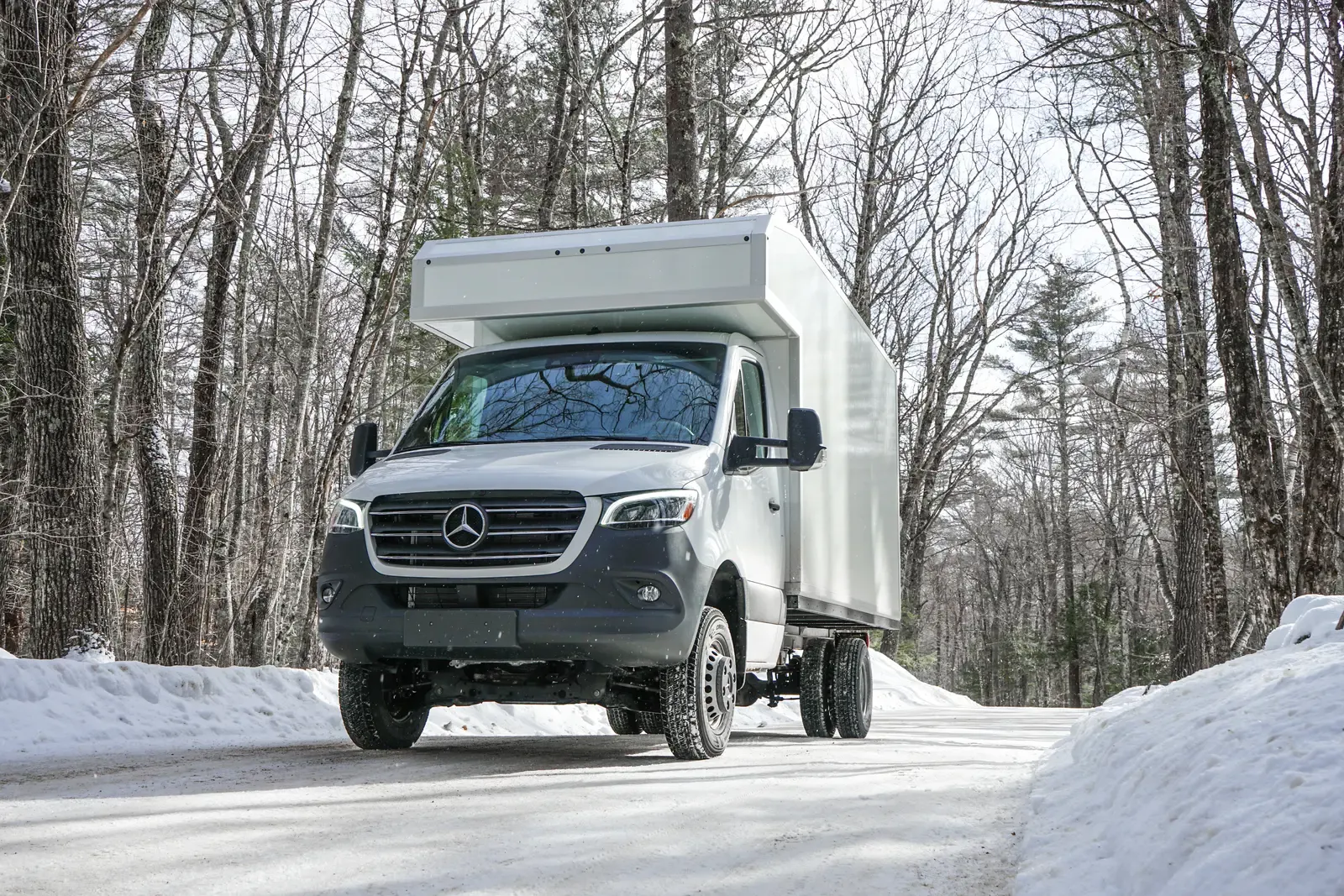 White composite box camper on a Mercedes-Benz Sprinter 170 driving a snowy forest road, front three-quarter view