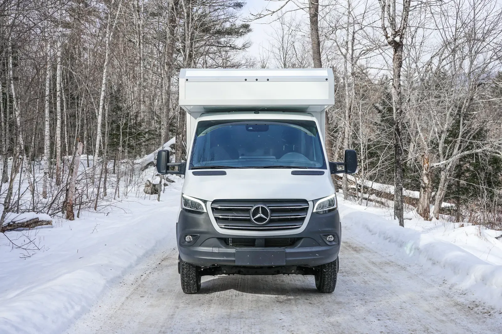 White composite box camper on a Mercedes-Benz Sprinter 170 among snowy trees, front three-quarter view