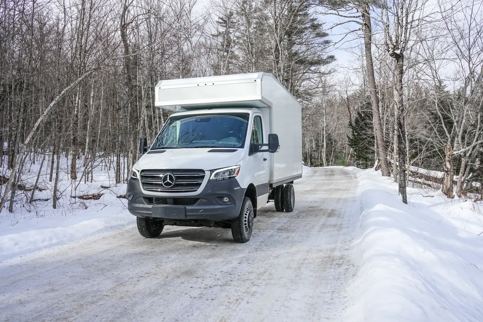 White composite box camper on an AWD Mercedes-Benz Sprinter 170 on a snow-covered road, front three-quarter view