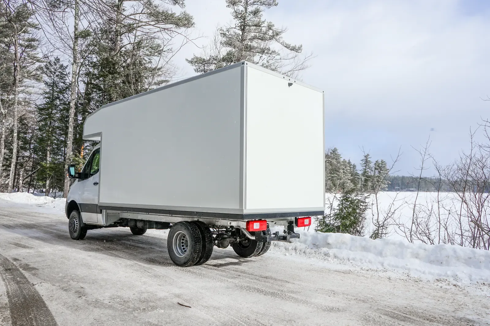 White composite box camper on a Mercedes-Benz Sprinter 170 driving away toward a frozen lake, rear three-quarter view